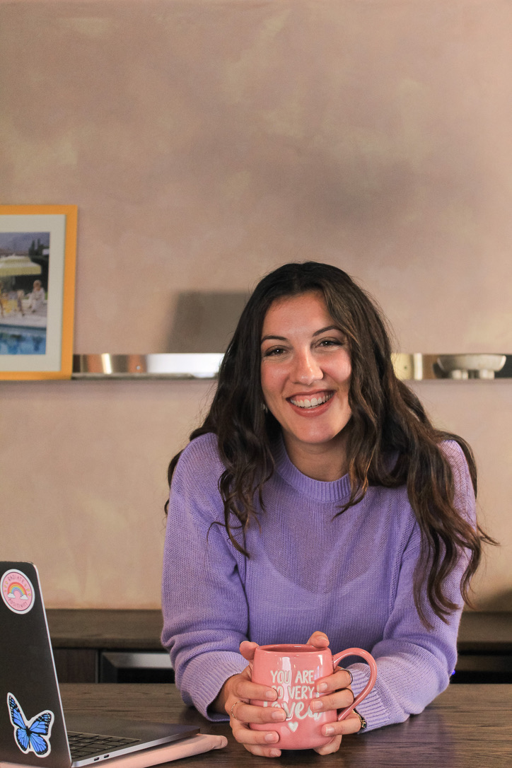 Francesca smiling at her desk, holding a mug that reads you are so very loved